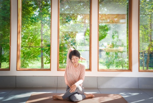 緑を望む部屋でゆったりヨガをする女性